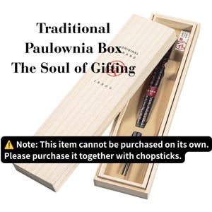 以下が含まれることがあります： スライド式の蓋が付いた明るい色の桐箱。Traditional Paulownia Box The Soul of Giftingという文字とISSOUのブランドロゴが印字されています。中には、赤い帯が付いた暗い色の柄入り箸がベージュの台紙に収められています。