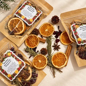 May include: Three clear pouches of holiday simmering potpourri featuring dried orange slices, cranberries, cinnamon sticks, and rosemary. Each label reads Holiday Simmering Potpourri with instructions. Loose dried ingredients are scattered nearby.