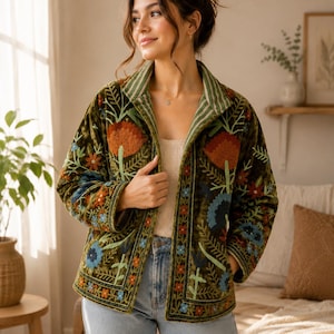 May include: An olive green velvet jacket featuring intricate floral embroidery in shades of orange, blue, and green. The jacket has a structured collar with a striped pattern on the inner lining, long sleeves, and a straight hemline.