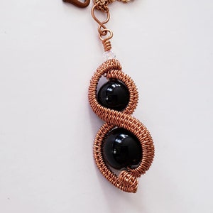 May include: A copper wire wrapped pendant necklace with two black onyx beads. The necklace has a heart-shaped clasp.
