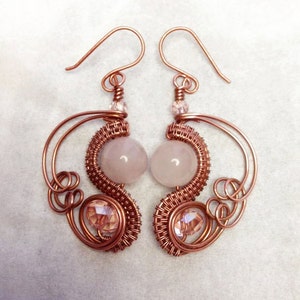 May include: A pair of rose gold wire wrapped earrings with pink and clear crystal beads. The earrings feature a delicate, swirling design.