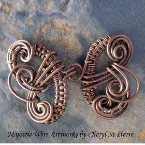 May include: A copper wire art piece in the shape of a butterfly with intricate swirls and woven details.  The piece is on a textured gray background.  Majestic Wire Artworks by Cheryl St. Pierre.