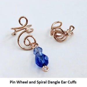 May include: A pair of gold-toned ear cuffs. One cuff is a simple spiral design, while the other is a pinwheel design with a dangling blue crystal.