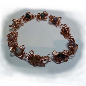 Peut inclure: Un bracelet en fil de cuivre avec une variété de pierres colorées. Les pierres sont enveloppées de fil de cuivre et sont reliées par une chaîne de fil de cuivre.