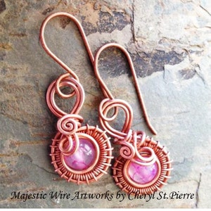 May include: A pair of copper wire earrings with pink gemstone accents. The earrings feature a delicate wire design with a swirl detail and a small pink gemstone in the center of each earring.