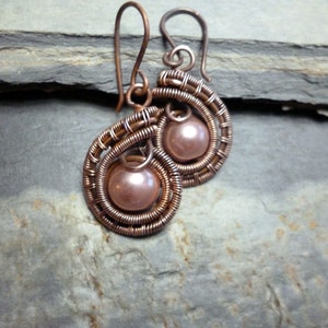 May include: A pair of copper wire earrings with a pink pearl bead in each. The earrings are handmade and have a delicate, intricate design.