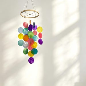 May include: A hanging mobile featuring a circular wooden frame with white strings suspending numerous translucent, circular discs in vibrant shades of red, orange, yellow, green, blue, and purple, creating a colourful, layered, and cascading display.