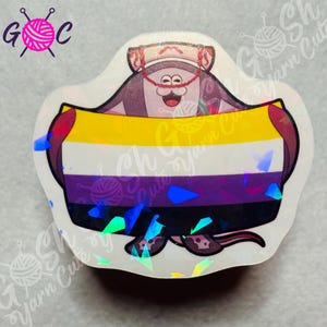 May include: Holographic sticker featuring a cartoon character holding a Non-Binary pride flag. The flag has yellow, white, purple, and black stripes. The character has a mustache and is wearing a hat. The sticker has the text "Gosh Yarn Cute" and "G C".