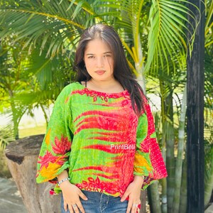 Könnte beinhalten: Ein locker sitzendes Langarmshirt mit einem lebendigen, grün-roten abstrakten Blumenmuster und sichtbaren weißen Steppnähten im Kantha-Stil. Das Kleidungsstück hat einen weiten Ausschnitt und wird mit einer blauen Jeans kombiniert. Der Text PrintBell ist sichtbar.