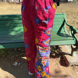 Può includere: Pantaloni rossi con un motivo geometrico blu, giallo e bianco. I pantaloni hanno un design cucito e una vita con coulisse. Il testo "PritBell" è visibile.