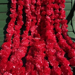 May include: A close-up of a collection of bright red garlands. The garlands are made up of many small, textured pieces, giving them a full and layered look. The lighting is good, showing off the deep red colour and the intricate details of the garlands.