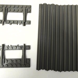 May include: Three gray plastic building toy components are arranged on a white surface. Two pieces have a rectangular base with vertical supports and a central opening. A third piece consists of multiple vertical rods.
