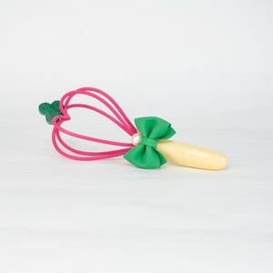 K&ouml;nnte beinhalten: Ein pinkfarbenes und gr&uuml;nes Massageger&auml;t mit herzf&ouml;rmigem Kopf. Das Werkzeug hat eine gr&uuml;ne Schleife mit Perlenakzent und einen hellgelben Griff. Der Kopf besteht aus rosa Gummi und hat einen gr&uuml;nen blattf&ouml;rmigen Akzent.