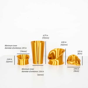 Puede incluir: Cuatro objetos cil&iacute;ndricos dorados con formas y aberturas variadas. Las dimensiones indicadas son: 62 mm de altura, 74 mm de di&aacute;metro interior, 172 mm de altura, 65 mm de di&aacute;metro interior, 102 mm de altura, y 8 cm de altura por 10 cm de ancho.