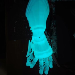 May include: A glowing, light blue articulated hand, possibly a prop or sculpture. The hand is detailed with visible joints and small circular perforations. The overall effect is futuristic and ethereal, with a strong visual impact against the dark background.