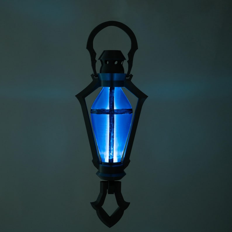 May include: An elaborate lantern with a bright blue interior. The lantern features a handle, decorative side panels, and a base. The blue light is a strong contrast to the dark frame, creating a striking visual.