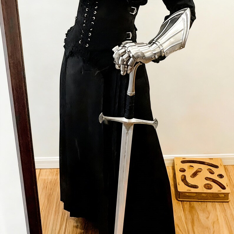 May include: A black outfit with a long skirt and corset, paired with silver gauntlets and a sword. The sword has a silver blade and a black wrapped handle. A wooden box with a carved design sits on the floor.