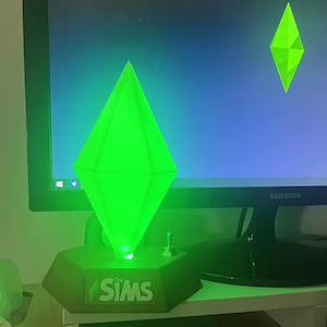 以下が含まれることがあります： ベースに「SIMS」の文字が入った、緑色に光るひし形のランプ。ランプはコンピューターモニターの前にあります。このランプは、ビデオゲームシリーズの象徴的なプランボブのレプリカです。