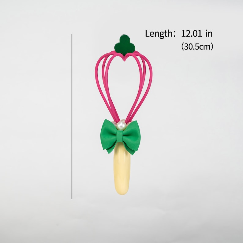 K&ouml;nnte beinhalten: Ein skurriler Zauberstab mit einem herzf&ouml;rmigen rosa Oberteil, einer gr&uuml;nen Schleife und einem Perlenakzent. Der Zauberstab ist 30,5 cm lang. Der Griff ist hellgelb.