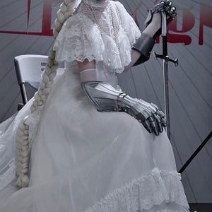 May include: A white dress with lace detailing and a long, thick braid. The person is wearing silver metal gauntlets and holding a sword. The background is a light gray with red text.