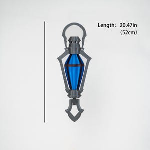 May include: A grey and blue decorative lantern, 52cm long. The lantern features a blue, teardrop-shaped centre with grey accents and a handle at the top. The base has a decorative, pointed design.