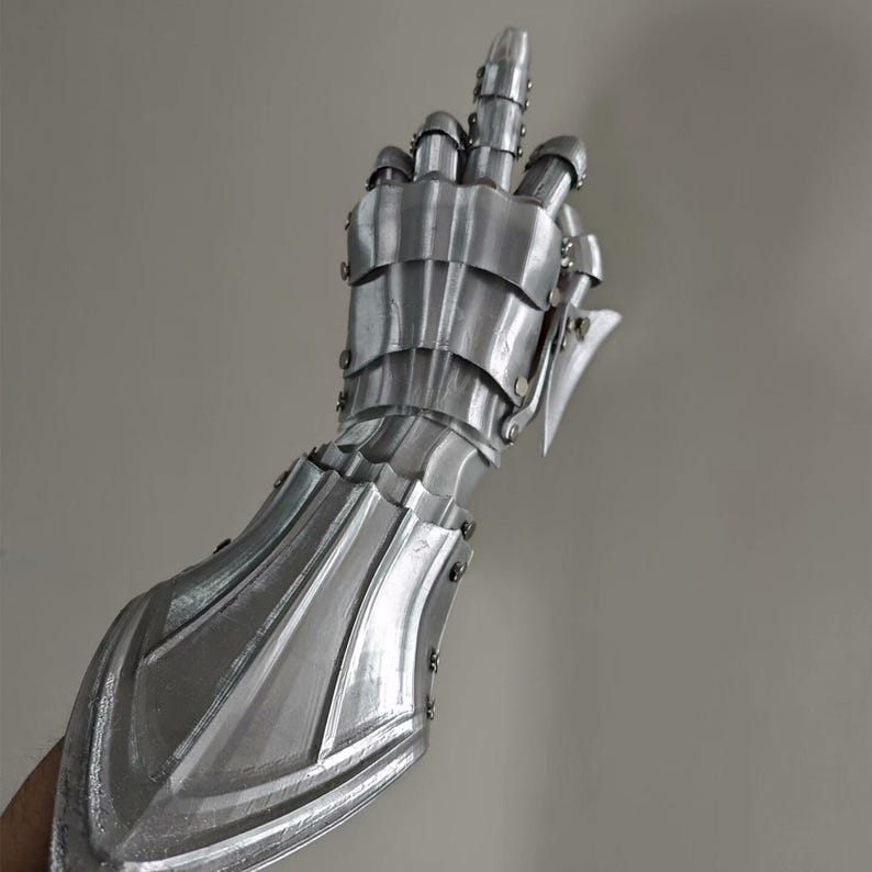 May include: A silver-colored articulated gauntlet, designed to cover the hand and forearm. The gauntlet is made of overlapping metal plates, with rivets and a pointed extension at the wrist. The fingers are also articulated.
