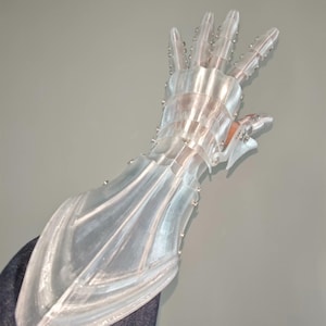 Puede incluir: Una mano protésica transparente y articulada con un diseño futurista. La mano está hecha de plástico transparente y presenta múltiples articulaciones y pequeños remaches metálicos. Los dedos están ligeramente curvados, y la estética general es mecánica y de ciencia ficción.