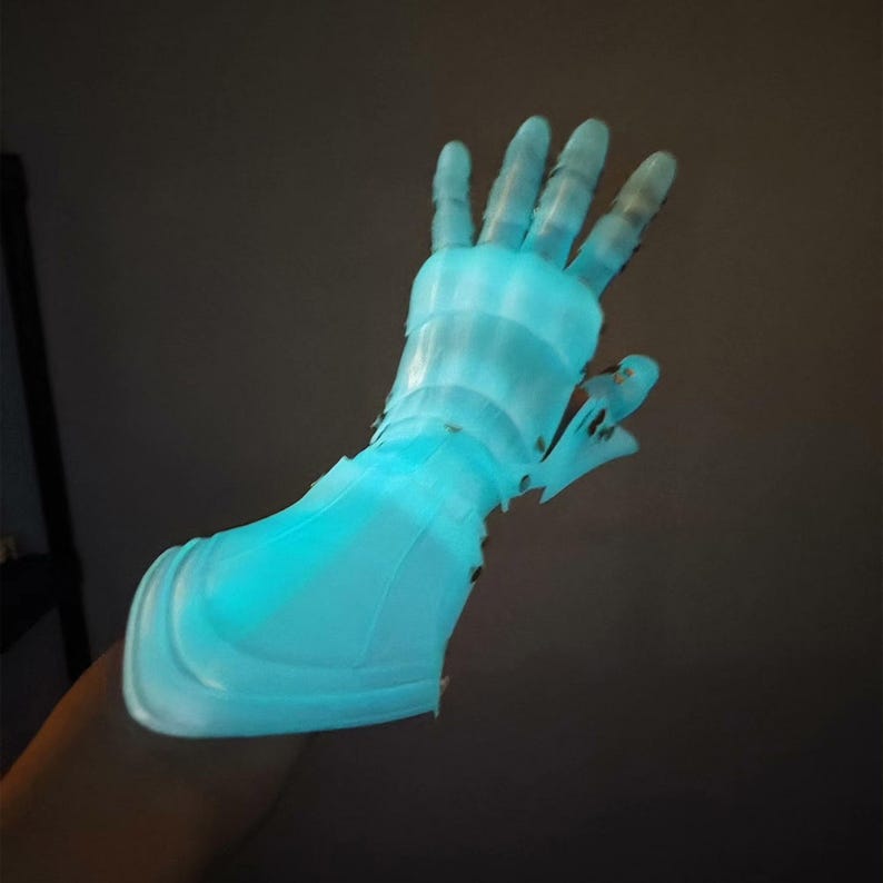 May include: A glowing, light blue prosthetic hand, possibly 3D-printed, with a detailed design. The hand is illuminated, creating a futuristic and technological aesthetic. The fingers are articulated, and the overall design suggests a focus on functionality and form.