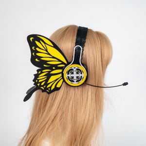 Puede incluir: Auriculares con diseño de ala de mariposa. La diadema negra tiene un ribete de encaje y un ala de mariposa amarilla y negra adjunta. Los auriculares son amarillos con un diseño blanco y un micrófono negro.