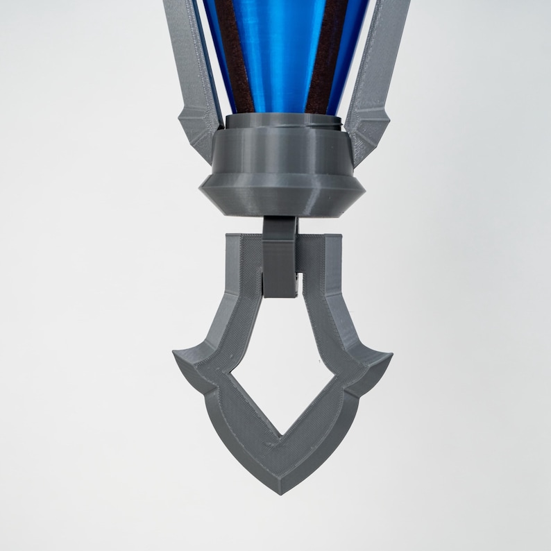 May include: A 3D-printed, grey and blue decorative object. The top section is blue with a dark brown band, connected to a grey, geometric base. The base has a diamond-shaped cutout at the bottom. The object is set against a white background.
