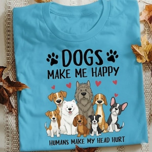 May include: A light blue t-shirt with the text "DOGS MAKE ME HAPPY" and "HUMANS MAKE MY HEAD HURT". The shirt features a graphic of several cartoon dogs and red hearts.