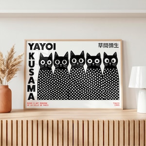 May include: A rectangular poster in a light wood frame featuring five black cats with large white eyes and white polka dots on their bodies. The text reads YAYOI KUSAMA, 草間彌生, MUSEE D ART MODERNE DE LA VILLE DE PARIS, and TOKYO 1995 in black and red.