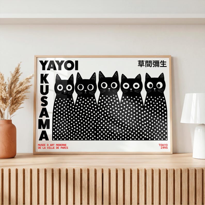 May include: A rectangular poster in a light wood frame featuring five black cats with large white eyes and white polka dots on their bodies. The text reads YAYOI KUSAMA, 草間彌生, MUSEE D ART MODERNE DE LA VILLE DE PARIS, and TOKYO 1995 in black and red.
