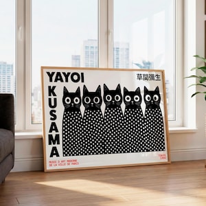 May include: A rectangular framed art print featuring five black cats with white polka-dot bodies and large white eyes. The text reads YAYOI KUSAMA, 草間彌生, MUSEE D ART MODERNE DE LA VILLE DE PARIS, and TOKYO 1995. The print has a white background and a light wood frame.