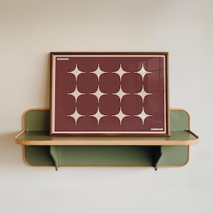 May include: A rectangular print in a dark wood frame featuring a deep maroon background with a repeating pattern of twelve off-white four-pointed stars. The text "BAUHAUS" is printed in small white letters in the top left and bottom right corners.