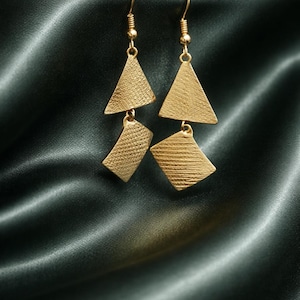 May include: Gold-colored dangle earrings with a geometric design. Each earring features a triangle shape at the top and a textured, rectangular shape below. The earrings hang from a gold-colored hook.