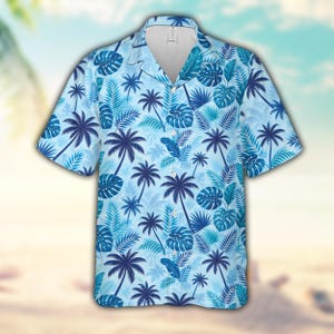 Peut inclure: Une chemise à manches courtes boutonnée avec un fond bleu clair et un motif répétitif de palmiers bleu foncé et de feuilles de monstera tropicales. Le vêtement présente un col classique, une patte de boutonnage et un ourlet droit.