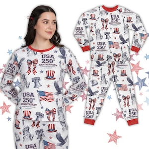 Könnte beinhalten: Weißes Pyjama-Set mit rotem Besatz, das den 250. Jahrestag der USA feiert. Das Design umfasst die amerikanische Flagge, die Freiheitsglocke, Adler und die Freiheitsstatue. Das Set besteht aus Oberteil und Hose.