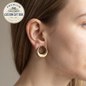 May include: A gold-colored crescent-shaped ear plug with black etched line details along the outer edge. The jewelry is worn in an earlobe piercing. A circular badge in the top left corner features a gift box icon and the text PREMIUM CUSTOM GIFT BOX TAILORED FOR YOU.