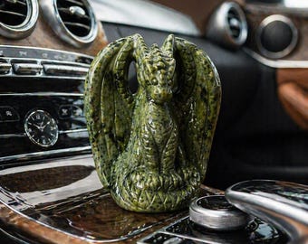 May include: A detailed green dragon figurine with textured wings and scales. The dragon is perched on a wooden surface, showcasing intricate craftsmanship. The figurine's color is a mottled green, adding to its fantasy aesthetic.