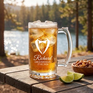 Könnte beinhalten: Ein klares Bierkrugglas gefüllt mit Eis und einem hellen Getränk. Der Krug hat einen Henkel und zeigt eine weiße Smoking-Grafik und den Namen "Richard" mit "Groomsman 27.02.2026" darunter. Der Krug steht auf einem Holztisch mit Limettenspalten und einer Schüssel Nüsse.