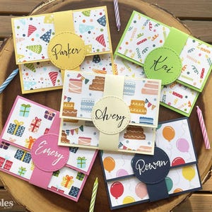 Puede incluir: Una colección de tarjeteros de cumpleaños personalizados con patrones coloridos y nombres. Cada tarjetero presenta un diseño único, que incluye sombreros de fiesta, pasteles, regalos y globos. Los nombres "Parker", "Kai", "Emery", "Avery" y "Rowan" se muestran.