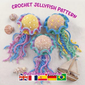 Pode incluir: Três águas-vivas de crochê em amarelo, azul, rosa e verde com bolinhas brancas. A imagem inclui o texto "CROCHET JELLYFISH PATTERN" e um pequeno veleiro de madeira. Conchas estão espalhadas ao redor das águas-vivas.