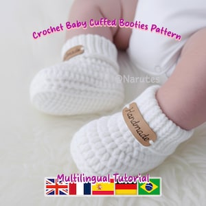 May include: White crochet baby booties with a cuffed design. Each bootie features a small, brown leather tag with the word "Handmade". The image also includes the text "Crochet Baby Cuffed Booties Pattern" and "Multilingual Tutorial".