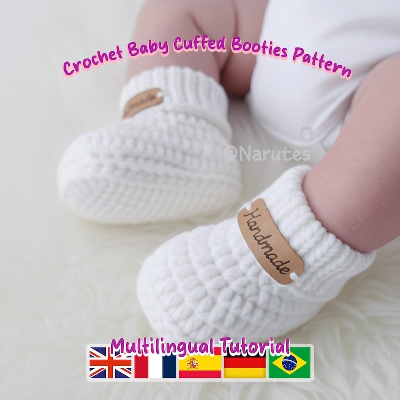 May include: A pair of white crochet baby booties with a cuffed design. Each bootie has a small, brown leather tag that reads "Handmade". The image also includes the text "Crochet Baby Cuffed Booties Pattern" and "Multilingual Tutorial".