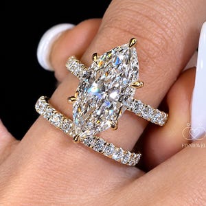 Op de afbeelding: Een gouden verlovingsringset met een grote marquise-geslepen centrale steen in een zeskantige zetting, vergezeld door een bijpassende ring. Beide ringen zijn bezet met kleine, in pavé gezette ronde diamanten voor een schitterende uitstraling.