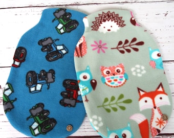 May include: Two blue and green fleece hot water bottle covers. One cover has a tractor pattern and the other has a woodland animal pattern with owls, foxes, and hedgehogs.