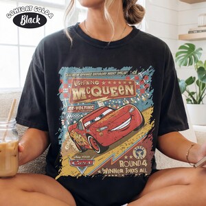May include: Black t-shirt featuring a graphic of Lightning McQueen from the Disney Pixar Cars movie. The design includes the text "Lightning McQueen" and "Cars", with a vintage, distressed aesthetic. The shirt is labeled "Comfort Color Black".