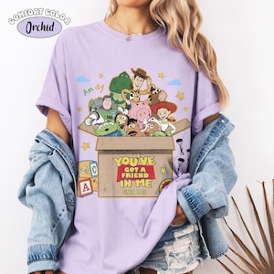 K&ouml;nnte beinhalten: Ein lila Comfort Colors T-Shirt mit einer Grafik von Toy Story-Charakteren. Das Design enth&auml;lt den Text "YOU'VE GOT A FRIEND IN ME SINCE 1995" und den Namen "Andy". Das Shirt hat kurze &Auml;rmel.