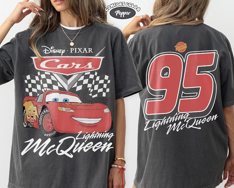 Może przedstawiać: Ciemnoszara koszulka z Lightning McQueen z filmu Auta Disneya i Pixara. Prz&oacute;d przedstawia postać z napisami "Cars" i "Lightning McQueen". Tył pokazuje duży napis "95" i "Lightning McQueen" w kolorze czerwonym.